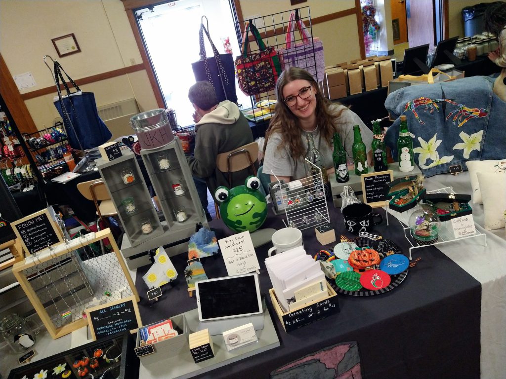 Joscelyn (smiling), sitting at her table at the Goodbye Winter Craft Fair 2023